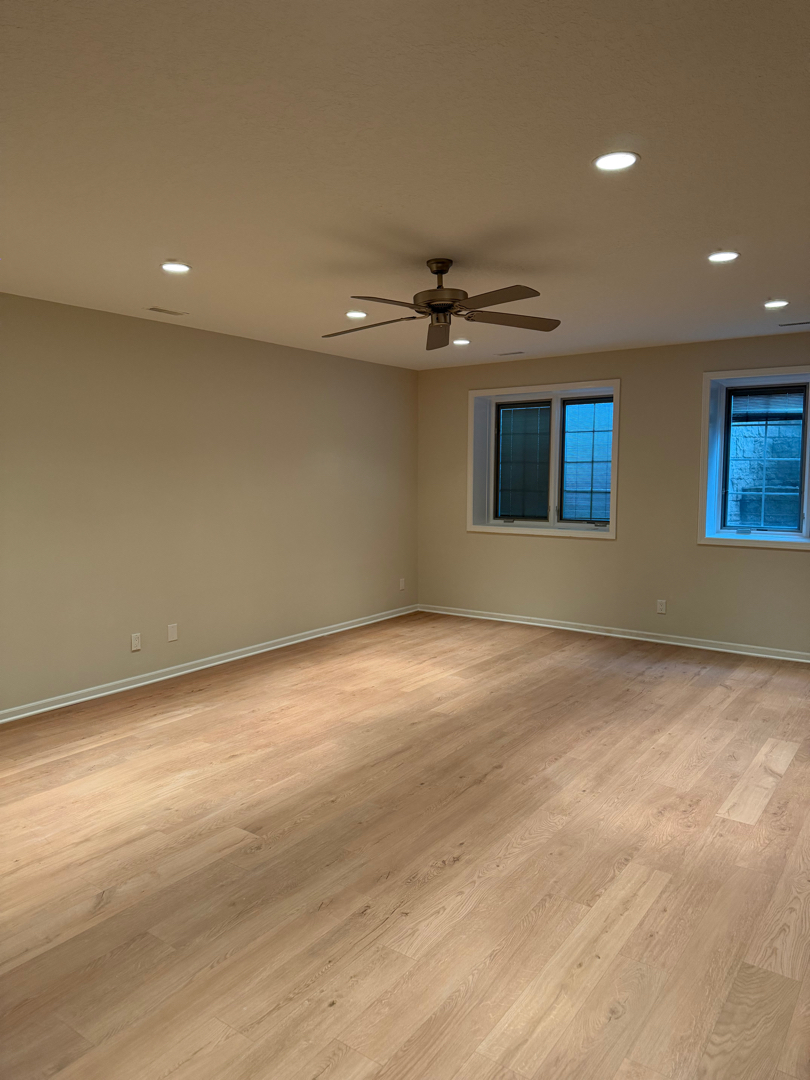 Fully finished basement family room with new flooring, paint, baseboards, and recessed lighting after water damage rebuild