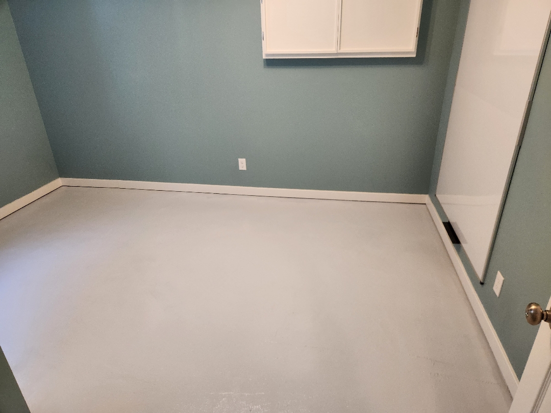 Rebuilt basement room with fresh teal paint, new baseboard, and prepped concrete floor ready for flooring